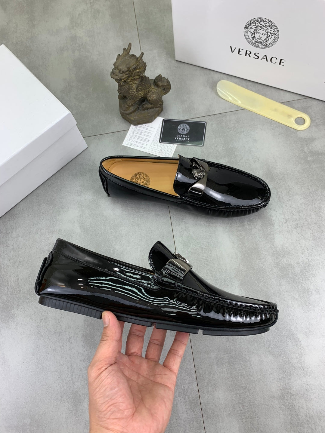 Black patent leather loafers with metal front emblem and slip-on silhouette