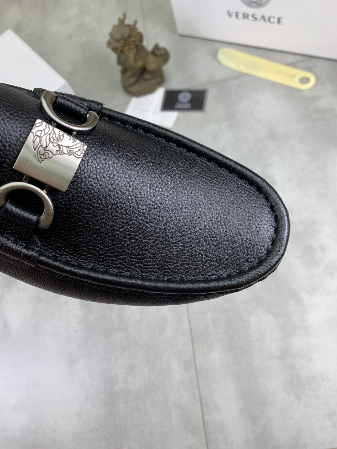Black leather loafer upper close-up with silver buckle and stitched edge