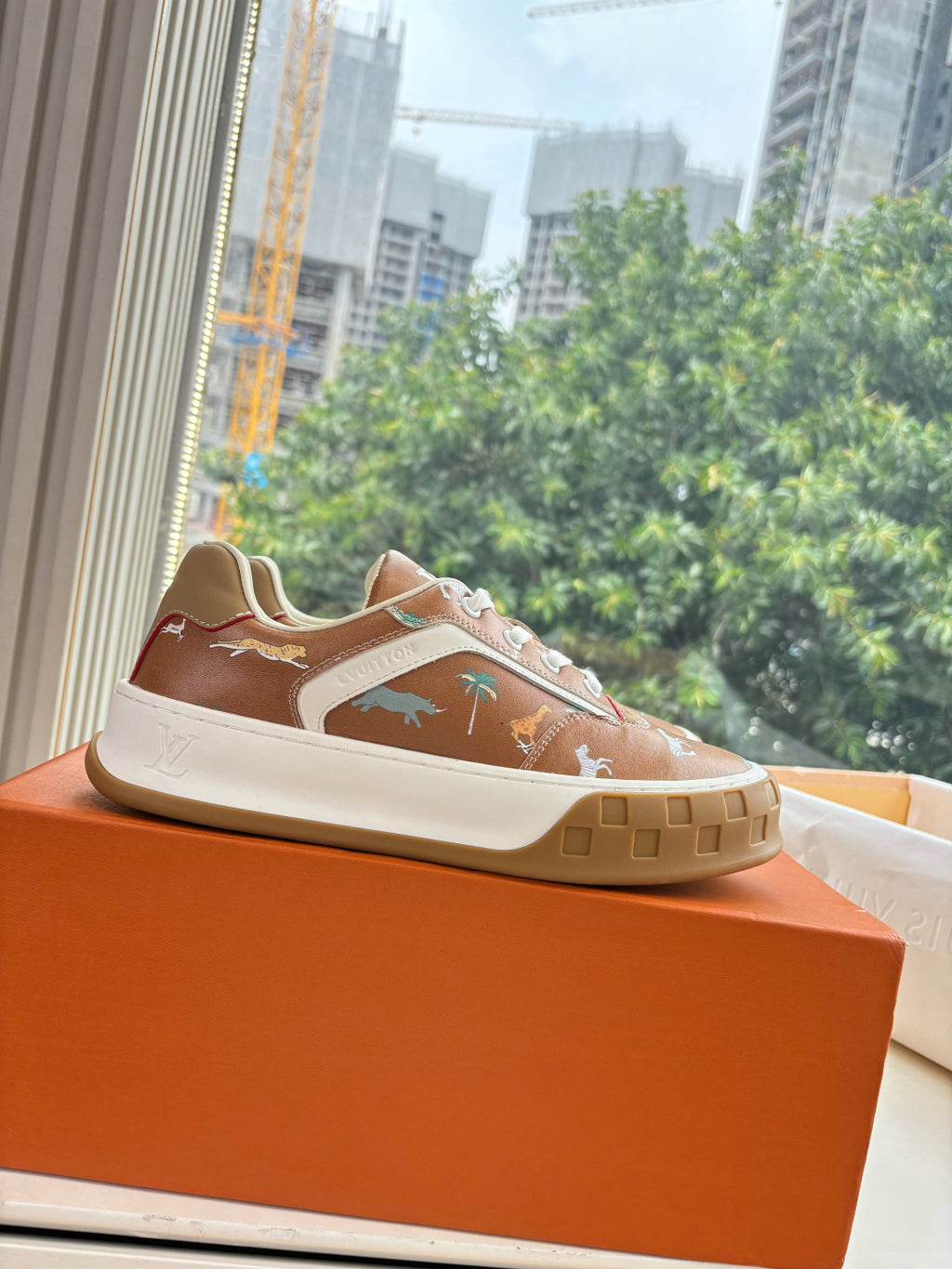 Louis Vuitton unisex sneakers on an orange box; brown uppers with white toe panel.