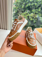 Louis Vuitton unisex sneakers held in hand, brown uppers with white laces and motifs.