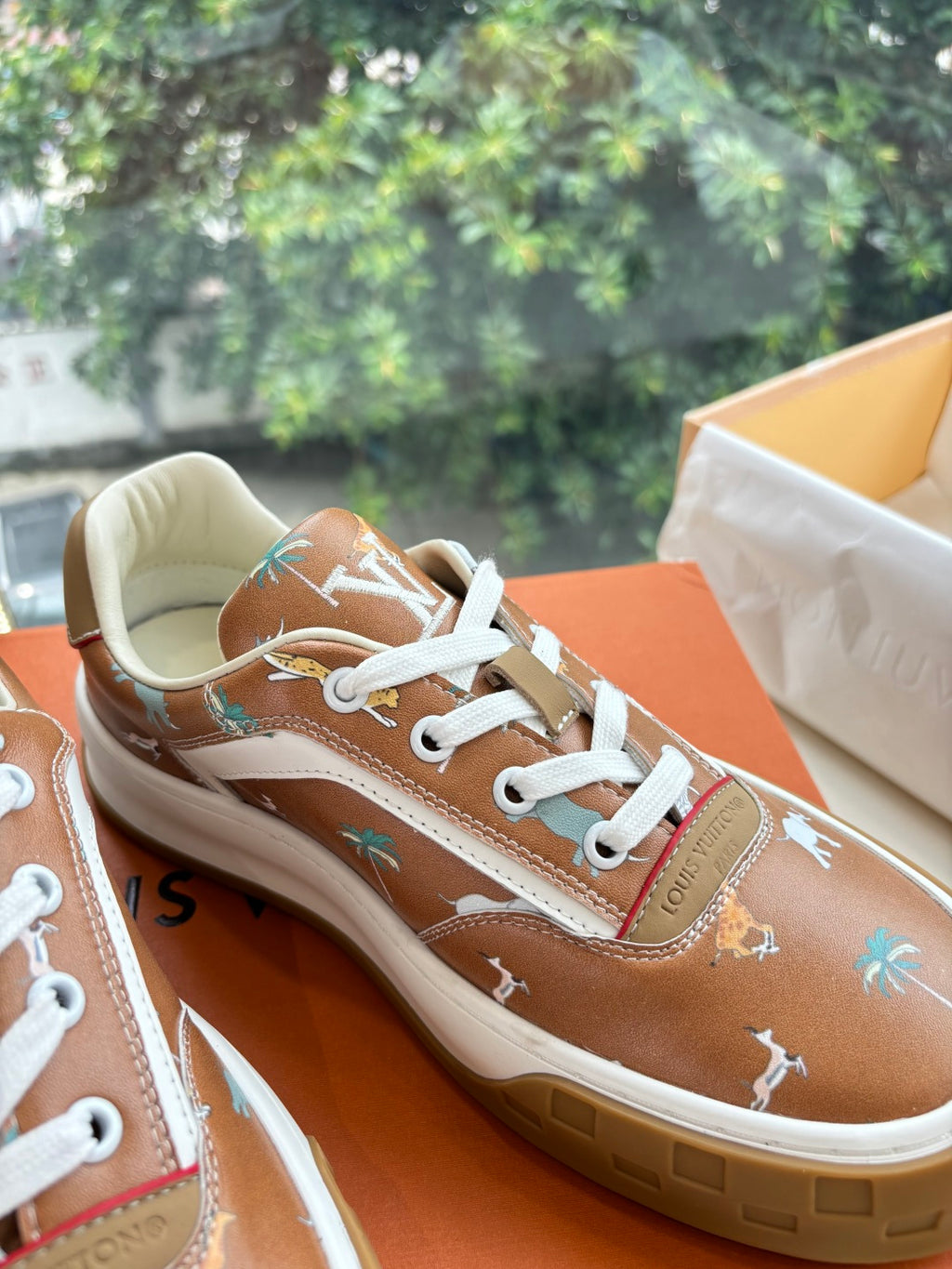 Louis Vuitton unisex sneakers close-up, brown with white laces and small printed motifs.