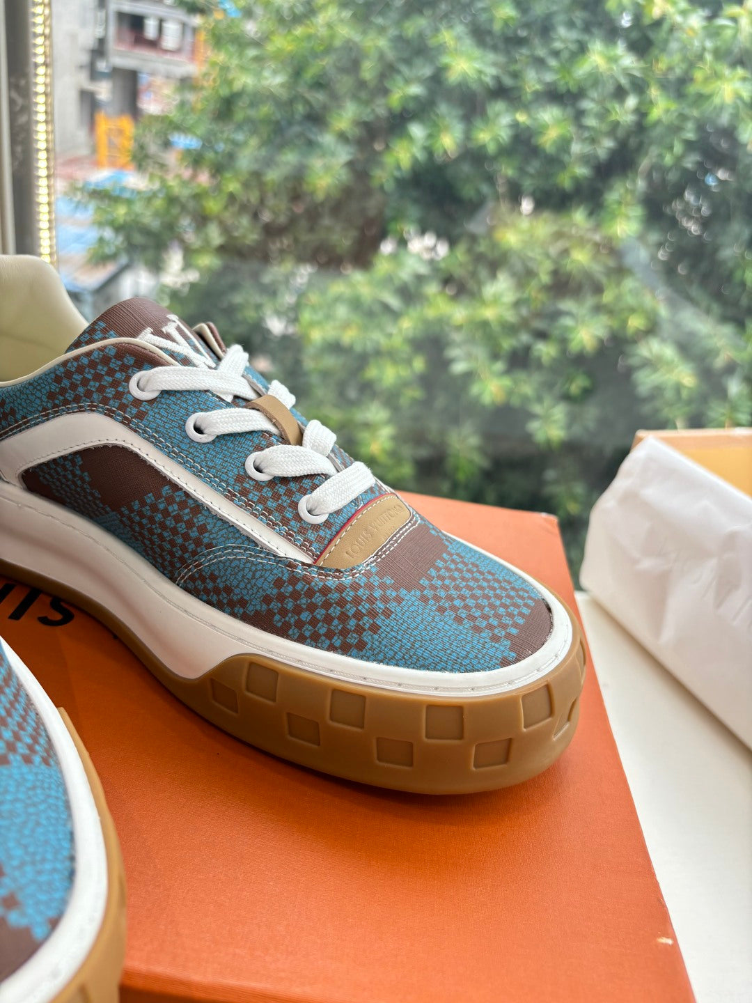 Louis Vuitton close-up of blue plaid sneaker upper with white laces and gum sole edge.
