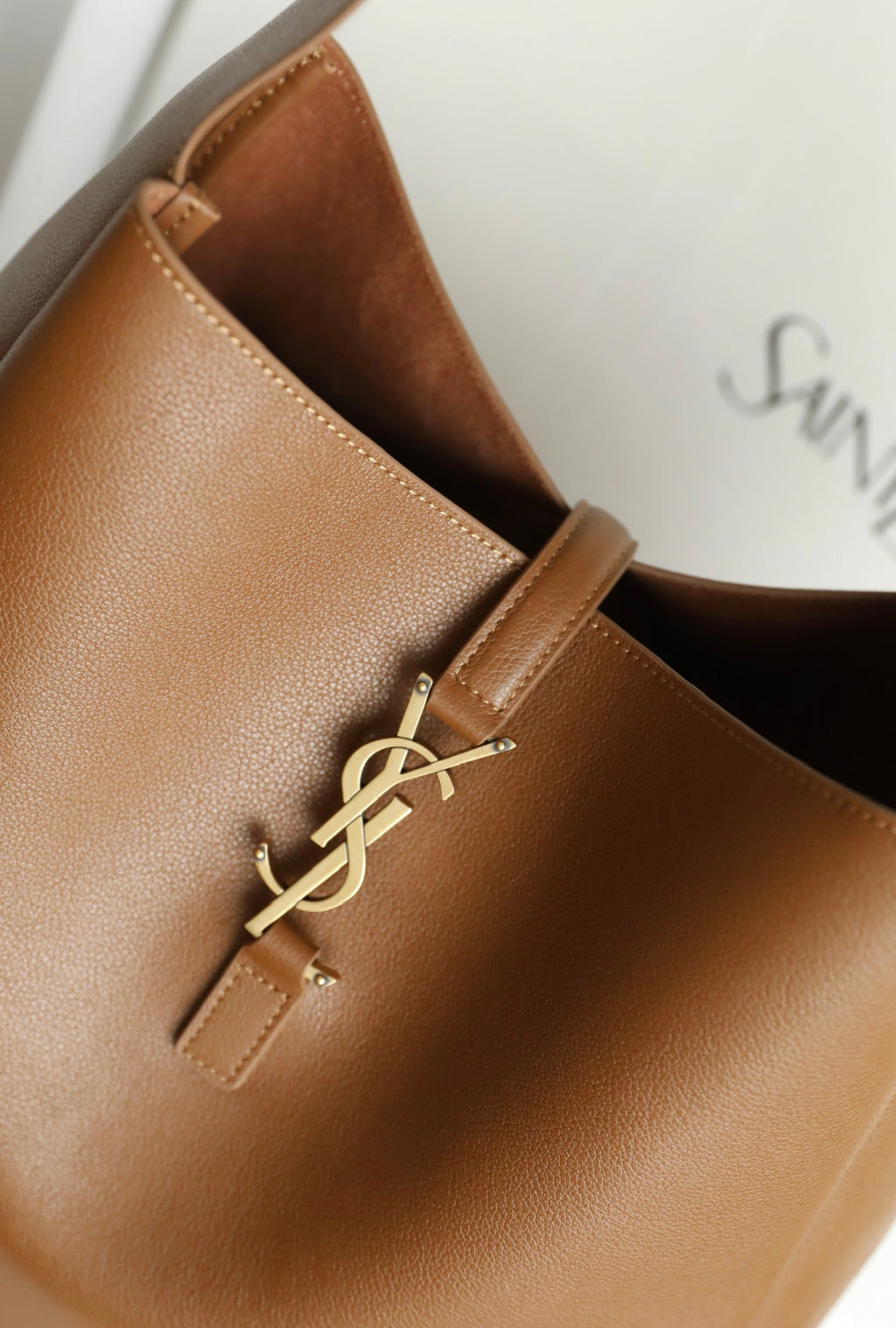 YSL brown leather bucket bag detail with gold YSL logo hardware and stitched strap