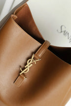 YSL brown leather bucket bag detail with gold YSL logo hardware and stitched strap