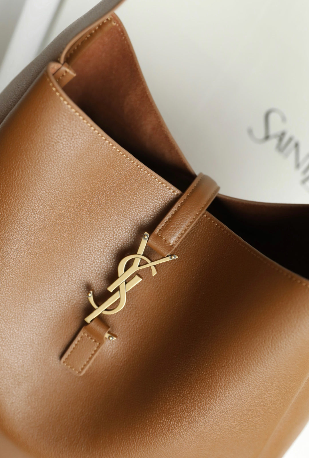 YSL brown leather bucket bag detail with gold YSL logo hardware and stitched strap