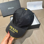 Black Prada baseball cap held in hand, gold “PRADA MILANO” logo and yellow trim