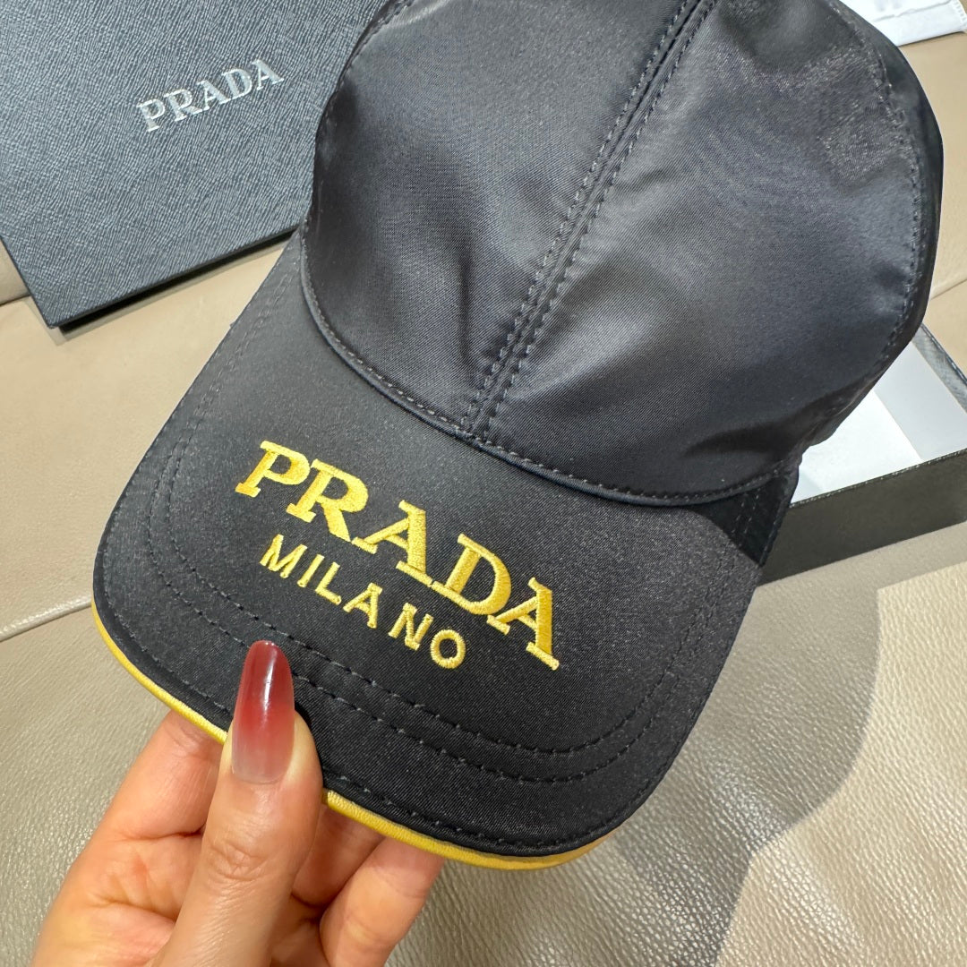 Black Prada baseball cap close-up, gold “PRADA MILANO” embroidery on front