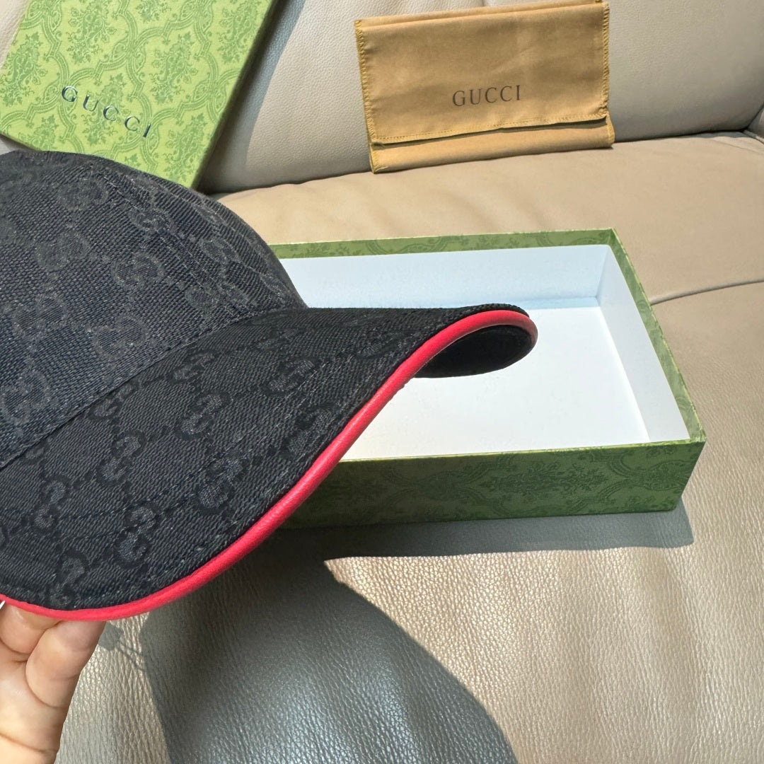Black GG-pattern baseball cap close-up showing curved brim with red underside trim.