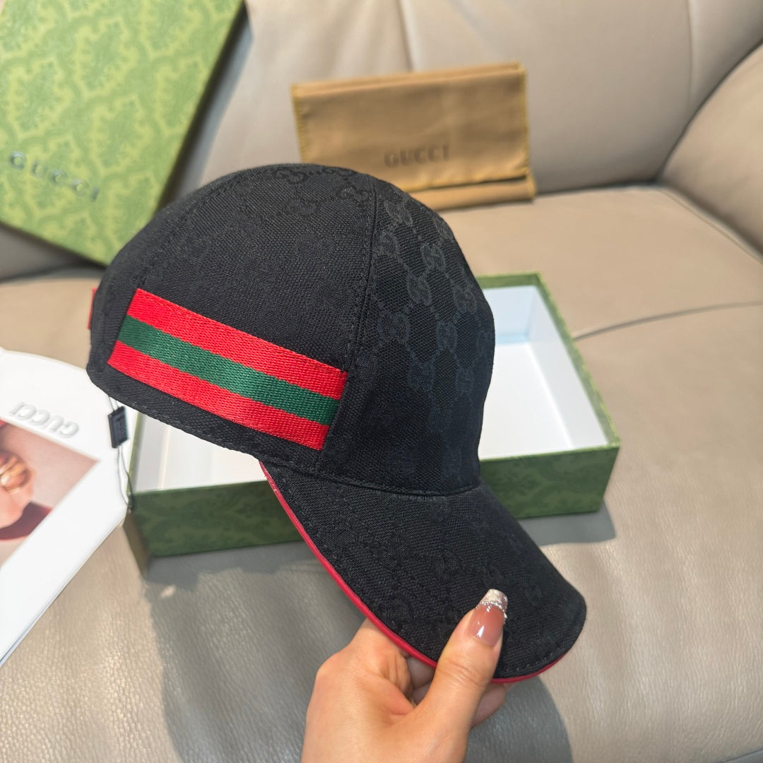 Black GG-pattern baseball cap with red and green Web stripe, held by brim edge.