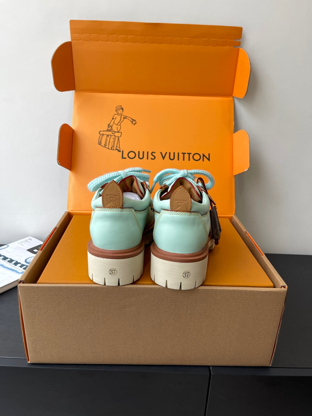 Pair of women's mint sneakers with blue laces and brown trim, back view in box