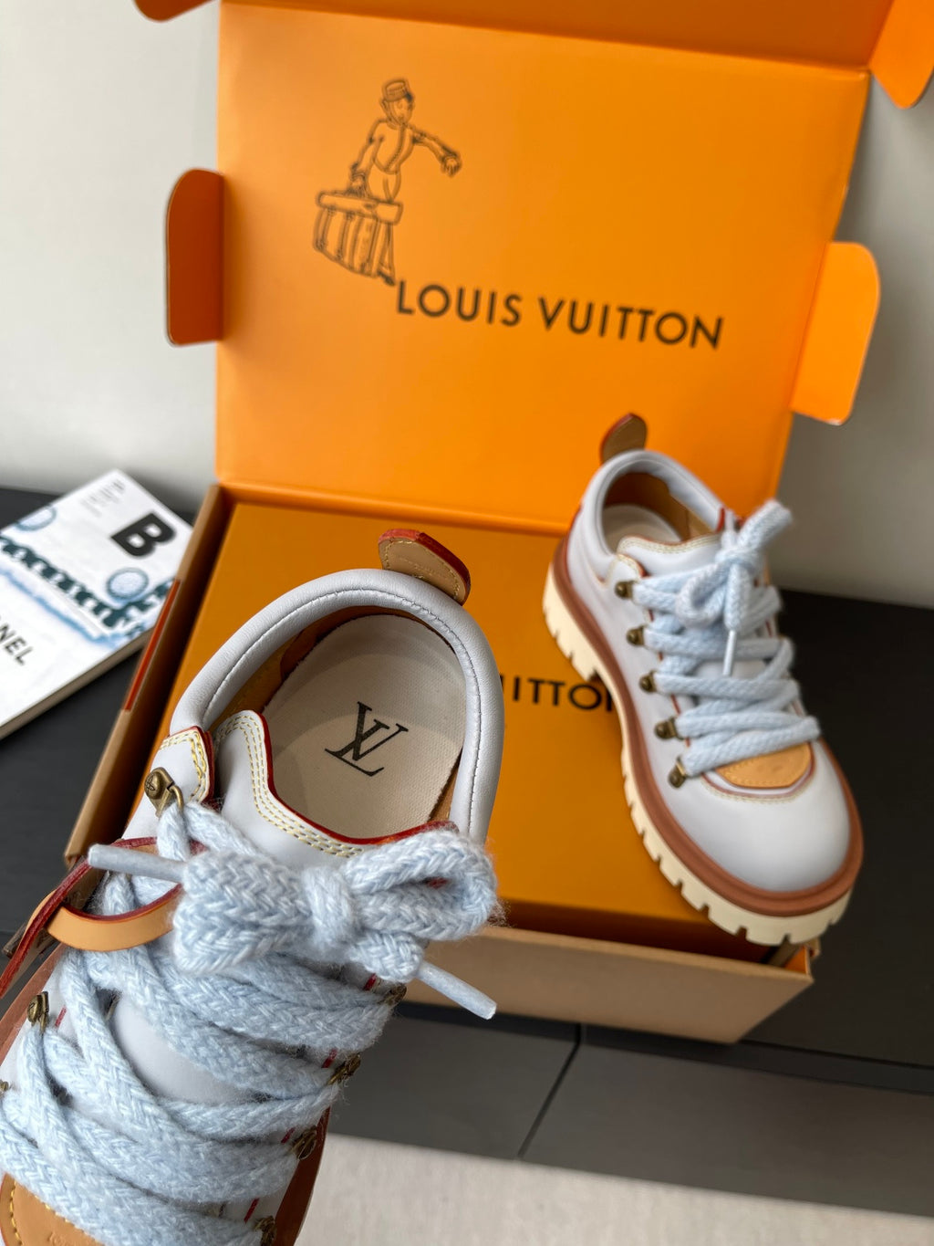 Women's white sneaker with blue laces, brown logo detail near tongue