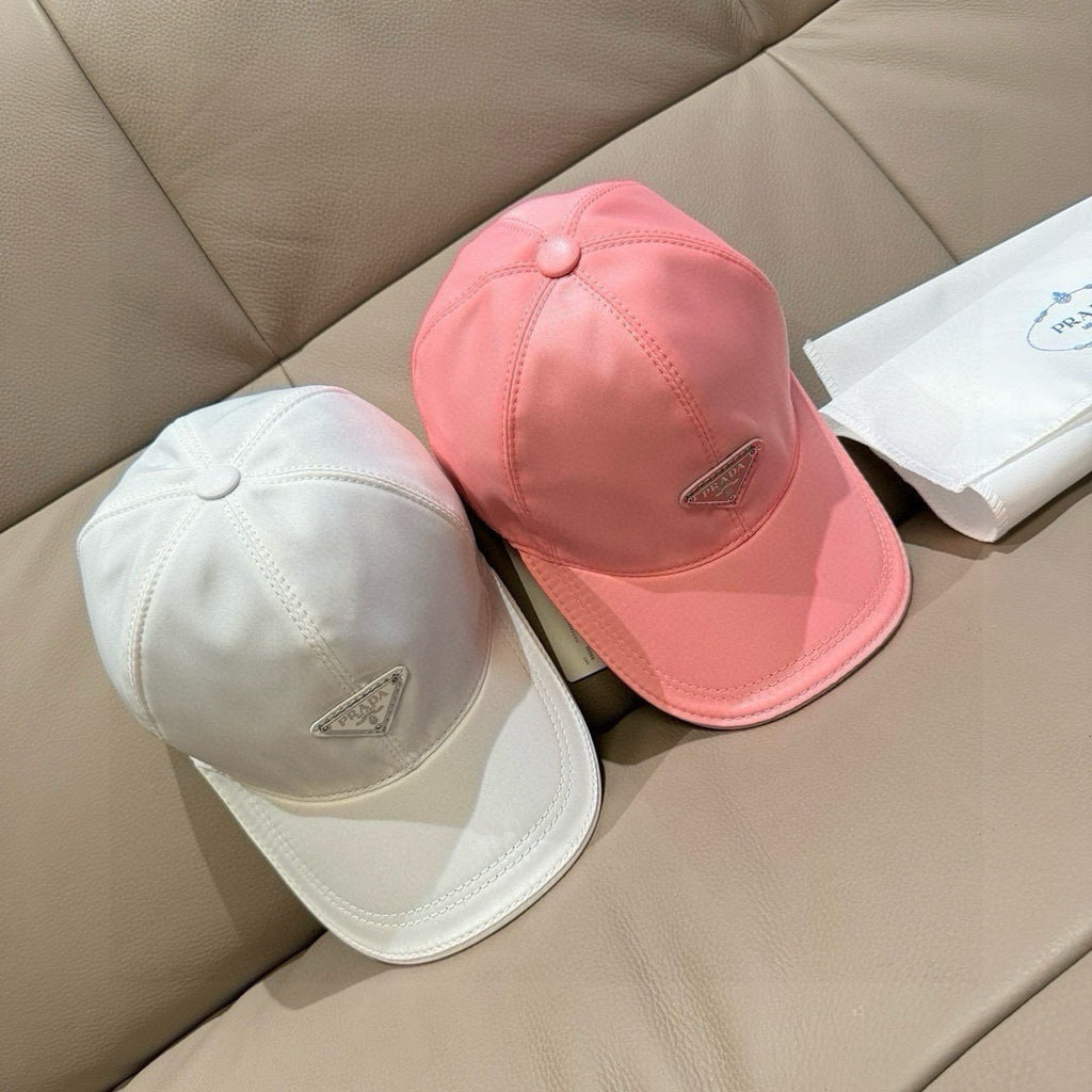 Prada cap pair: pink and white, each with triangular logo patch and curved brim.