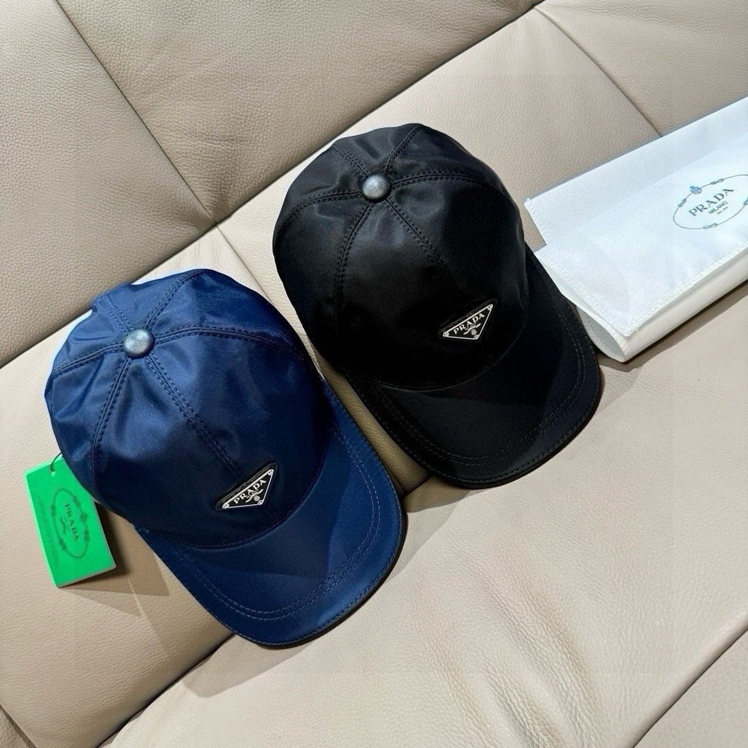 Prada caps pair: dark blue and black baseball caps with triangular front logo patches.