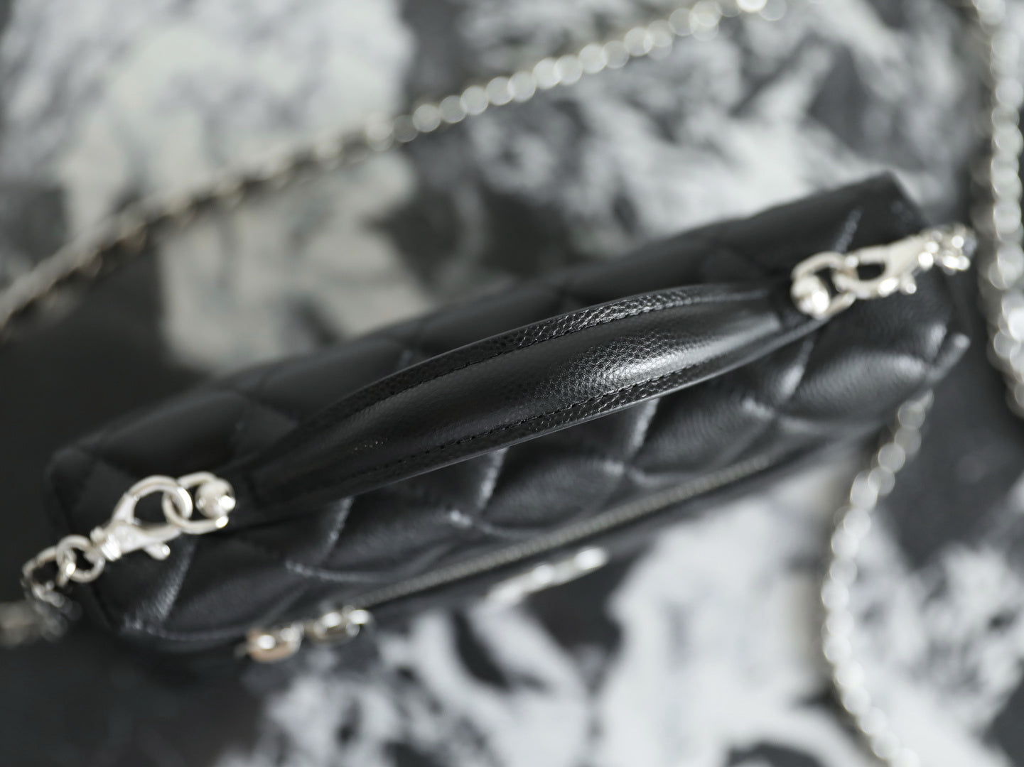 Close-up of chain strap and Chanel clasp on black quilted leather