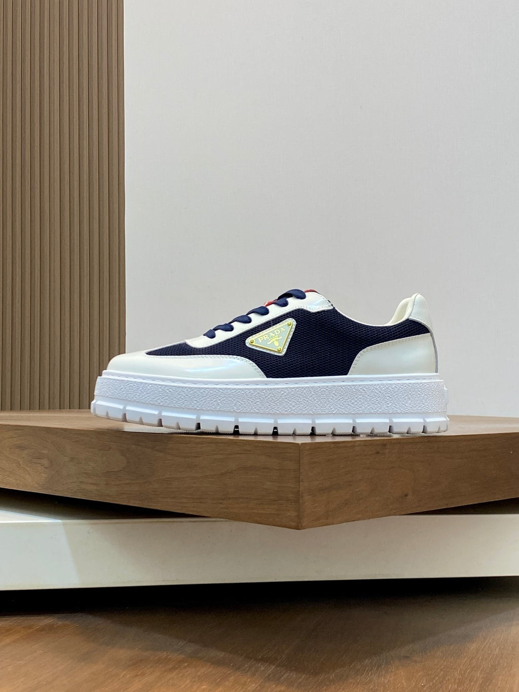 Unisex sneakers in white and navy with red lace accents and a gold triangular logo
