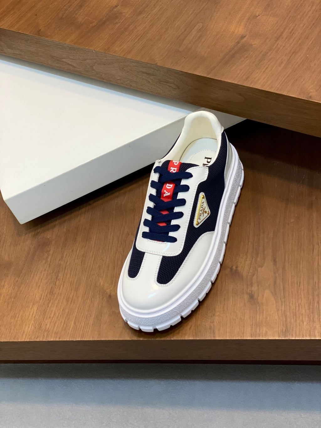 Single unisex low-top sneaker in white and navy with red laces and gold triangular logo