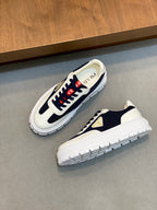 Unisex sneakers angled view in white and navy with red laces and gold logo triangle