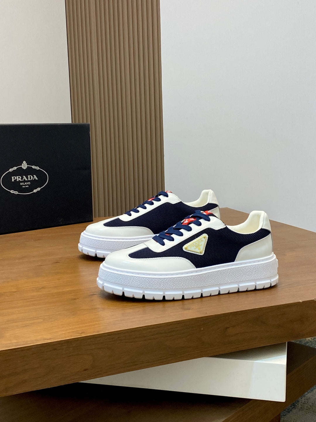 Pair of unisex low-top sneakers in white and navy with red laces and gold triangle emblem