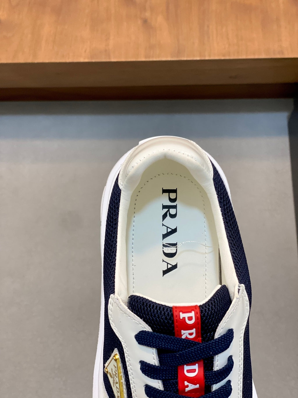 Unisex sneaker tongue view with Prada text and red logo patches on navy-and-white upper