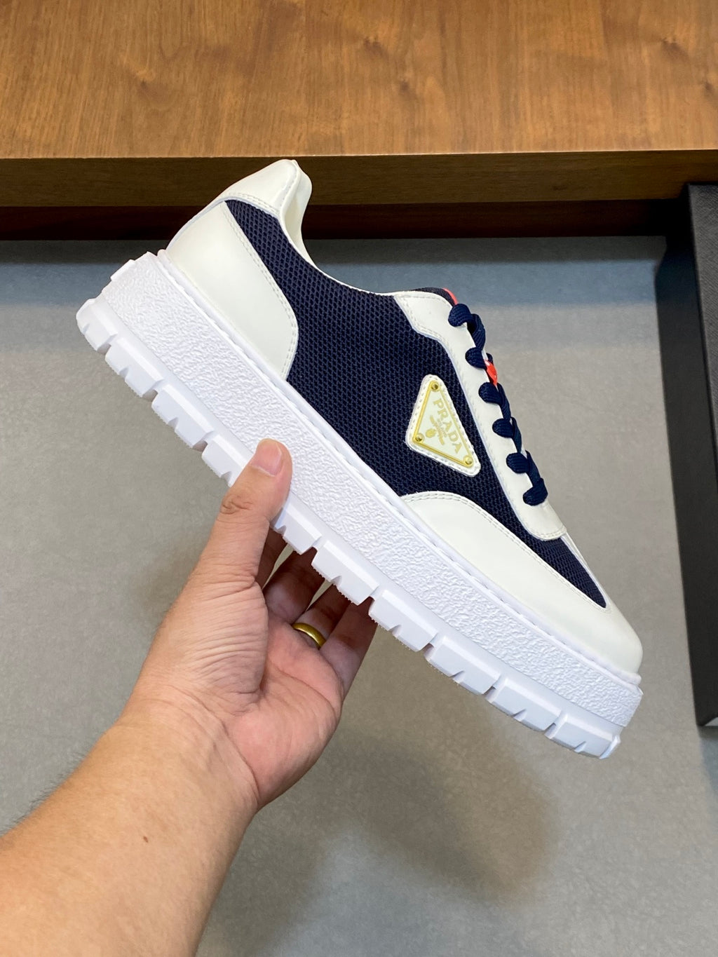 Unisex sneaker close-up in white and navy with red lace detail and gold triangular logo
