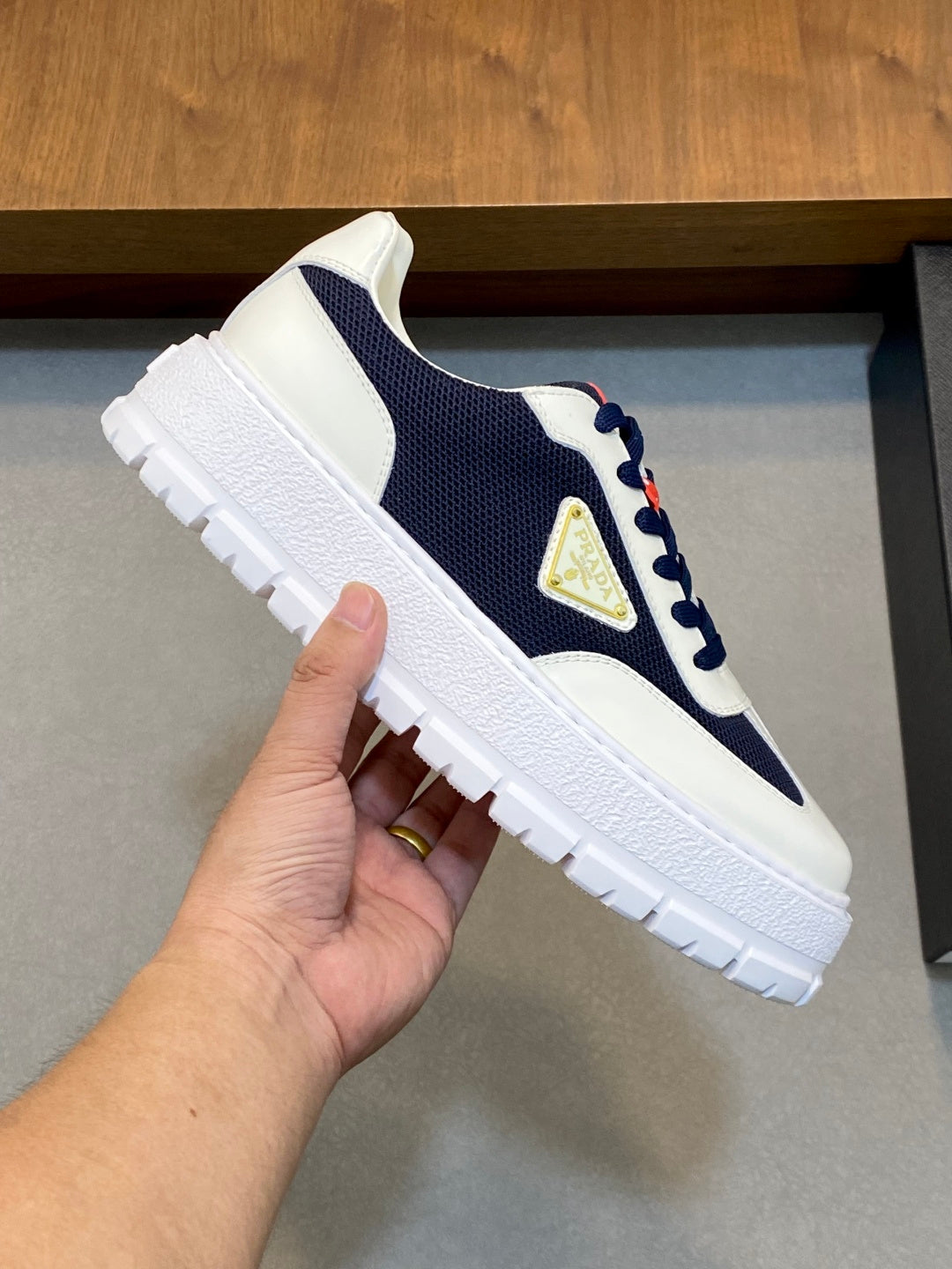 Unisex sneaker close-up in white and navy with red lace detail and gold triangular logo