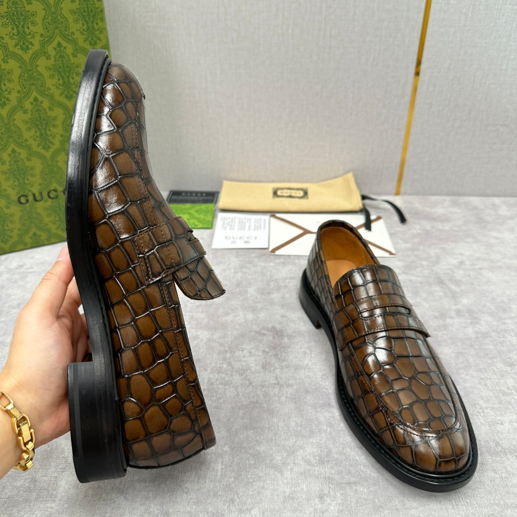 Pair of brown crocodile-embossed Gucci loafers in side profile, with black soles