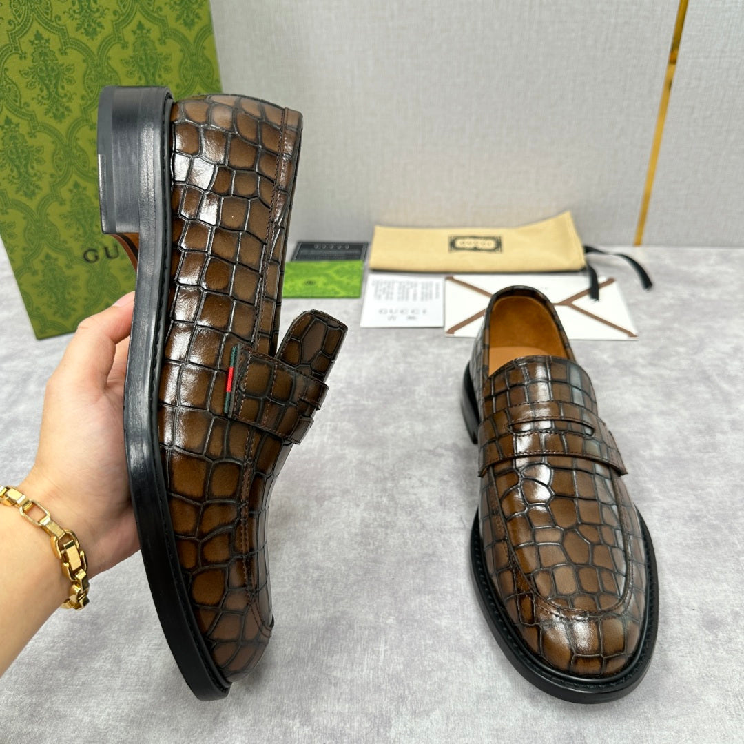 Brown crocodile-embossed Gucci loafers, one held near side sole and another front