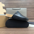 Black leather slide sandal with tan cork sole, stacked on textured base
