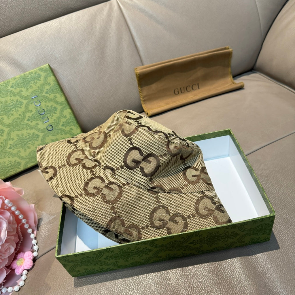 Tan GG monogram bucket hat with curved brim, laid on box with packaging nearby