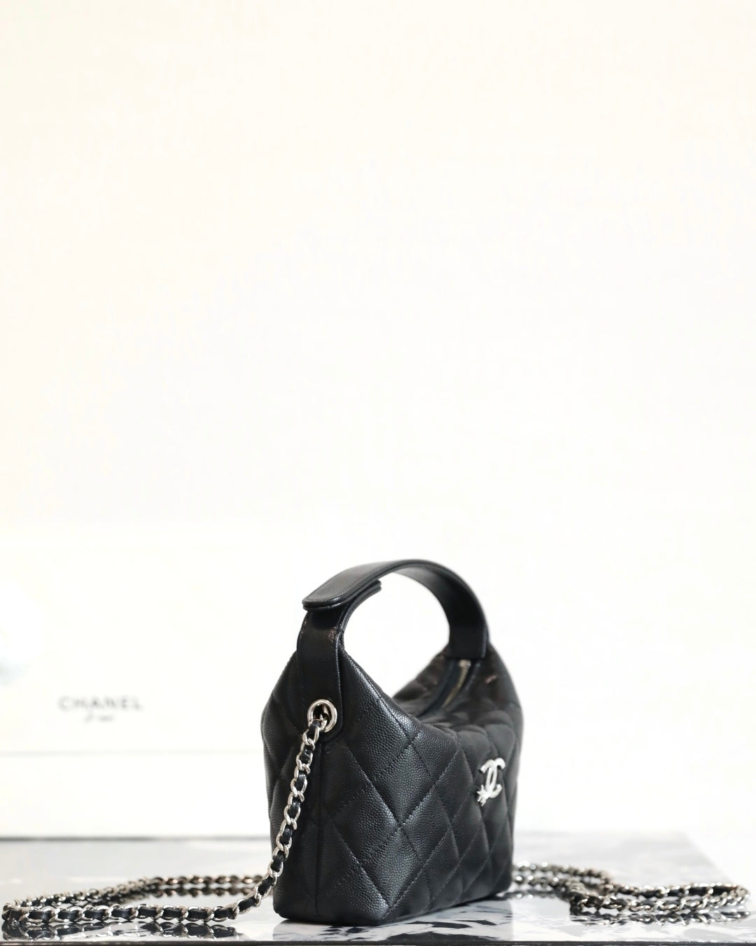 Black quilted mini handbag with chain strap and Chanel emblem, side view