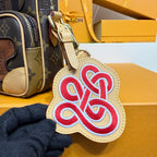 Monogram mini crossbody bag with heart-shaped embroidered charm on beige backing.
