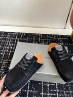 Black suede lace-up sneakers with tan lining, placed on shoebox