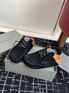 Black suede lace-up sneakers in open shoebox, tan insoles visible