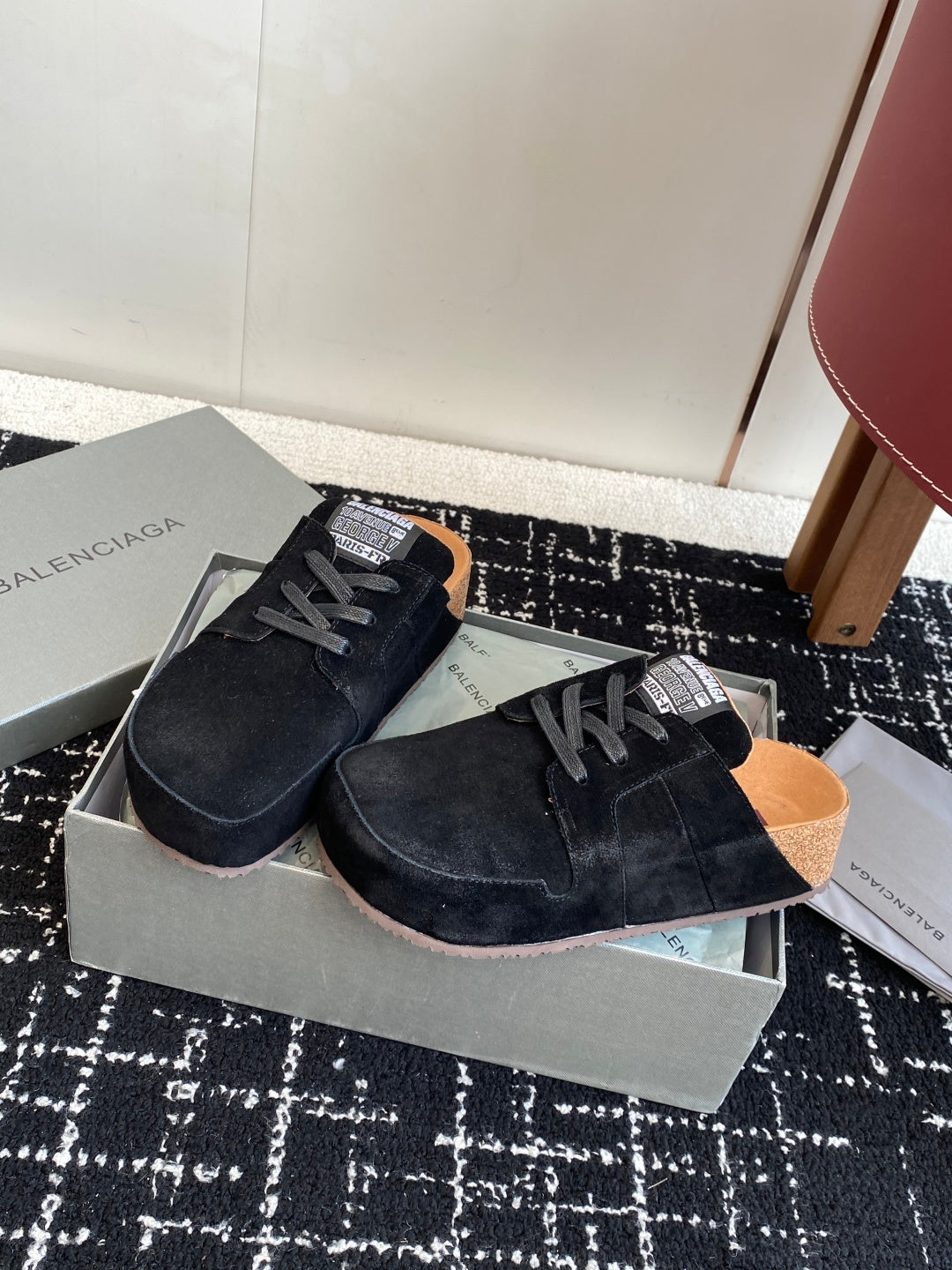 Black suede lace-up sneakers in open shoebox, tan insoles visible