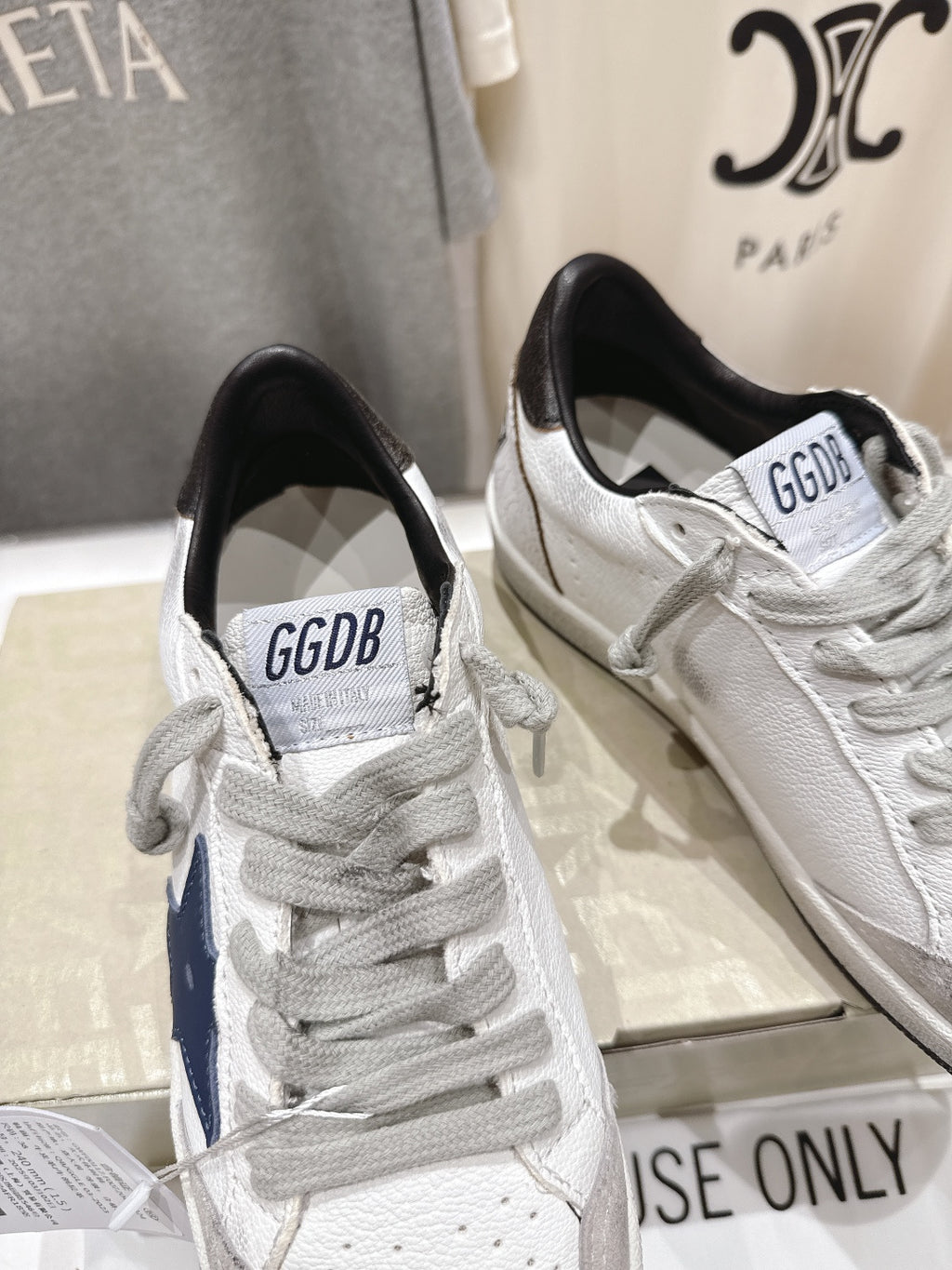 White luxury sneakers with gray laces and perforated toe; navy side stripe detail