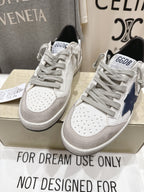 Pair of white luxury sneakers with gray laces, perforated toe, and navy side trim