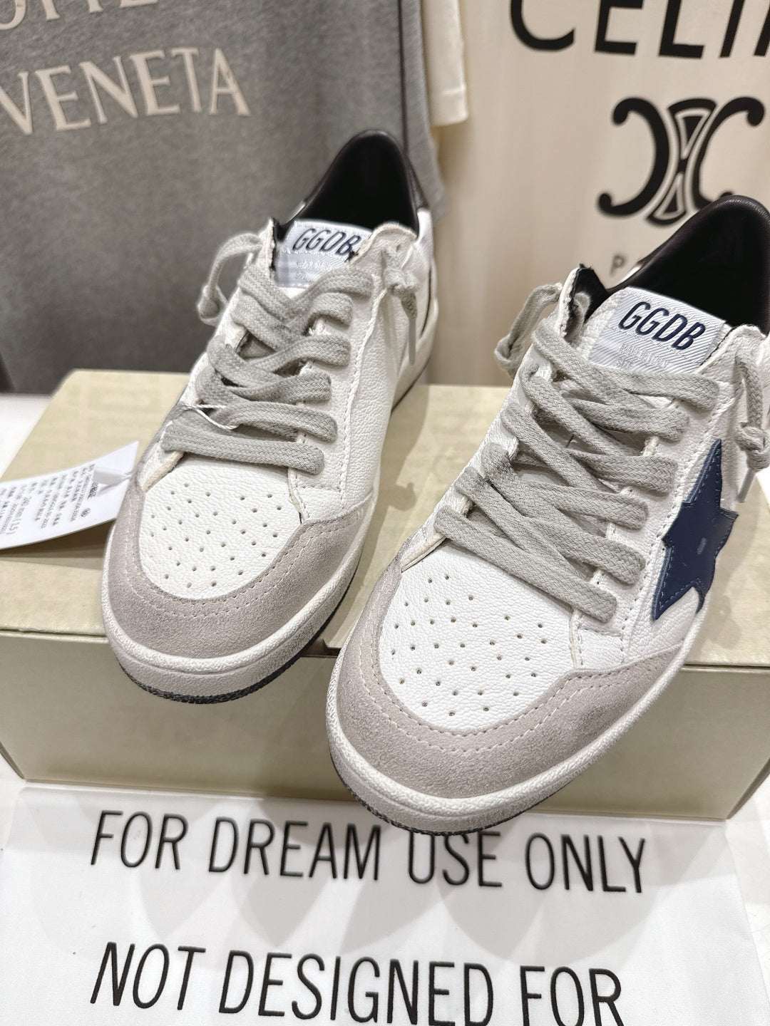 Pair of white luxury sneakers with gray laces, perforated toe, and navy side trim