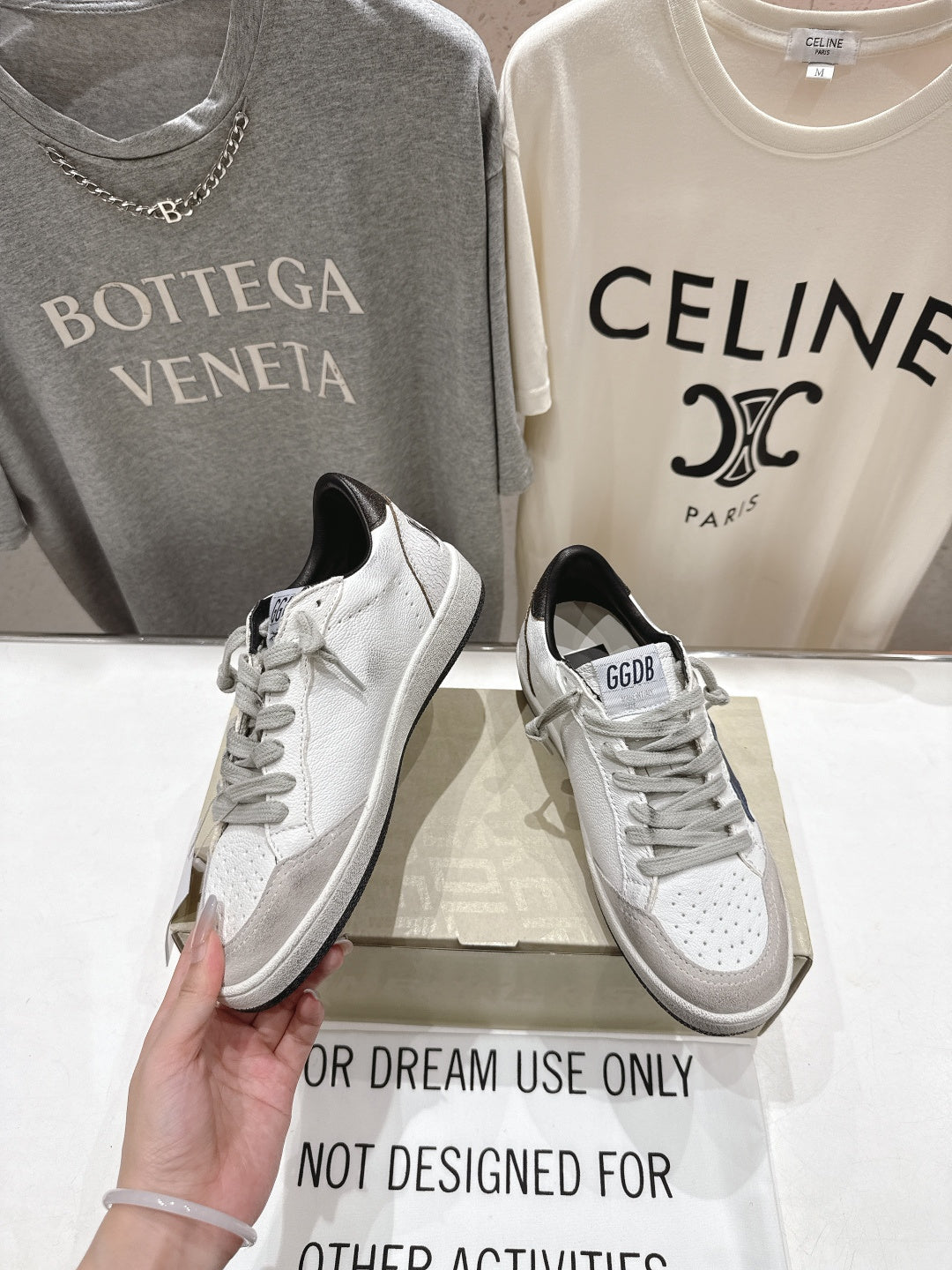 White luxury sneakers with gray laces and perforated toe, held in hand