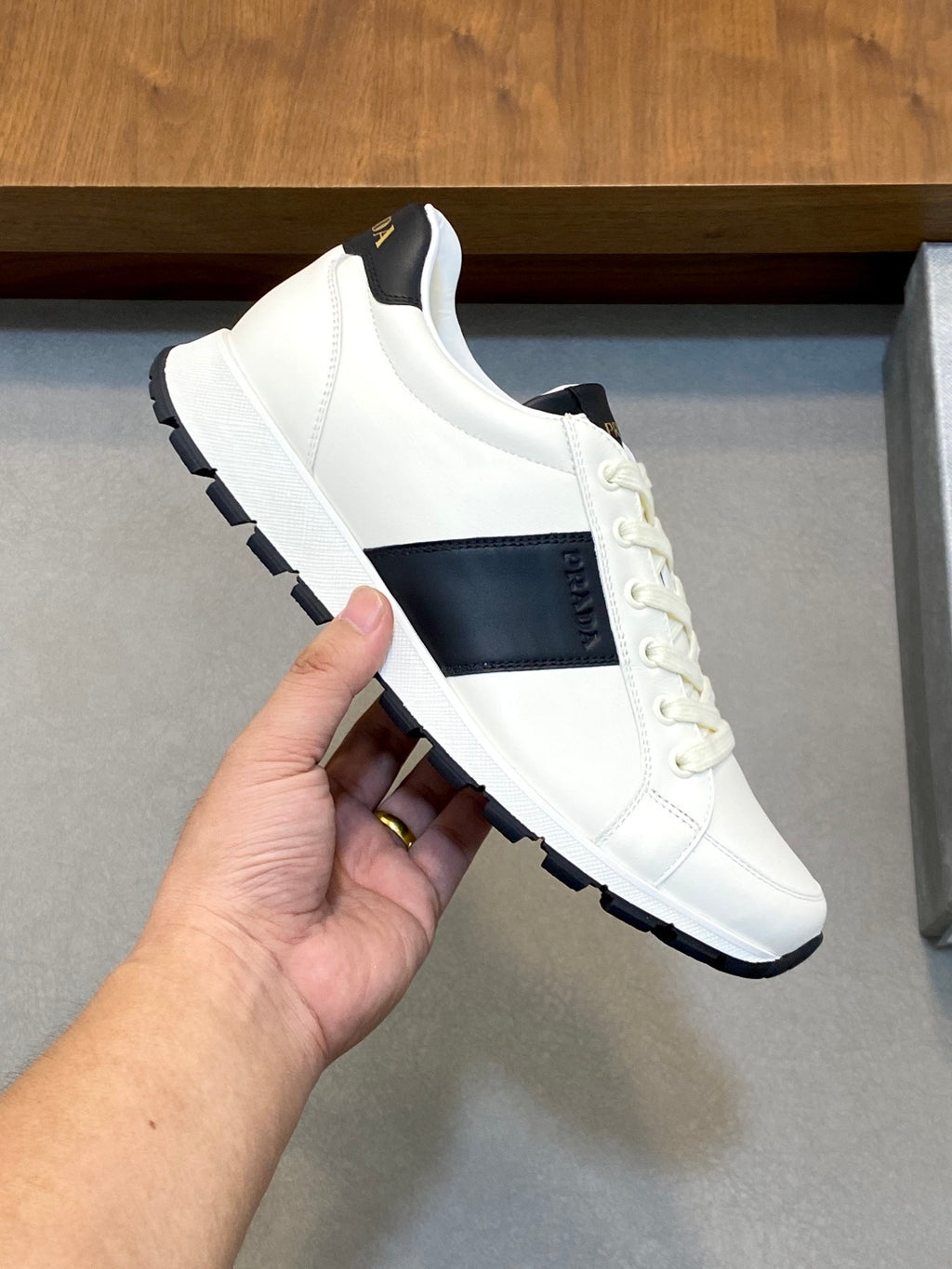 White low-top sneaker held by hand; black side band and lace-up closure