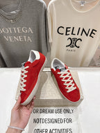 Golden Goose red sneakers with white laces and white sole, one shoe held near side