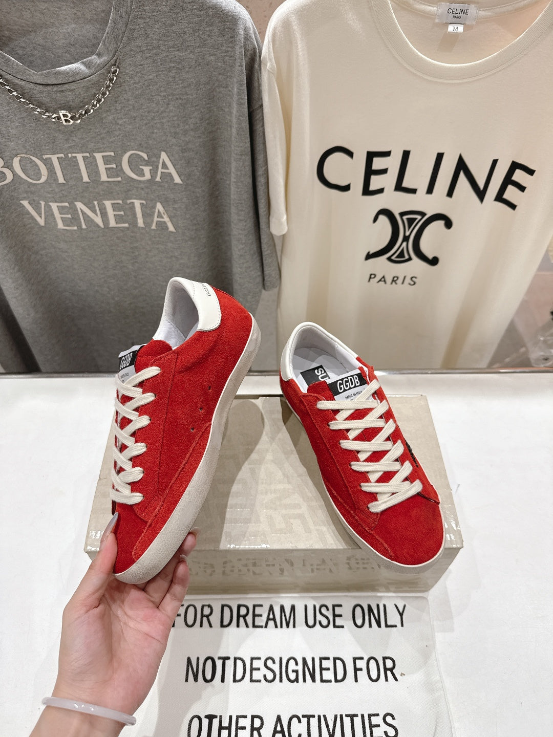 Golden Goose red sneakers with white laces and white sole, one shoe held near side