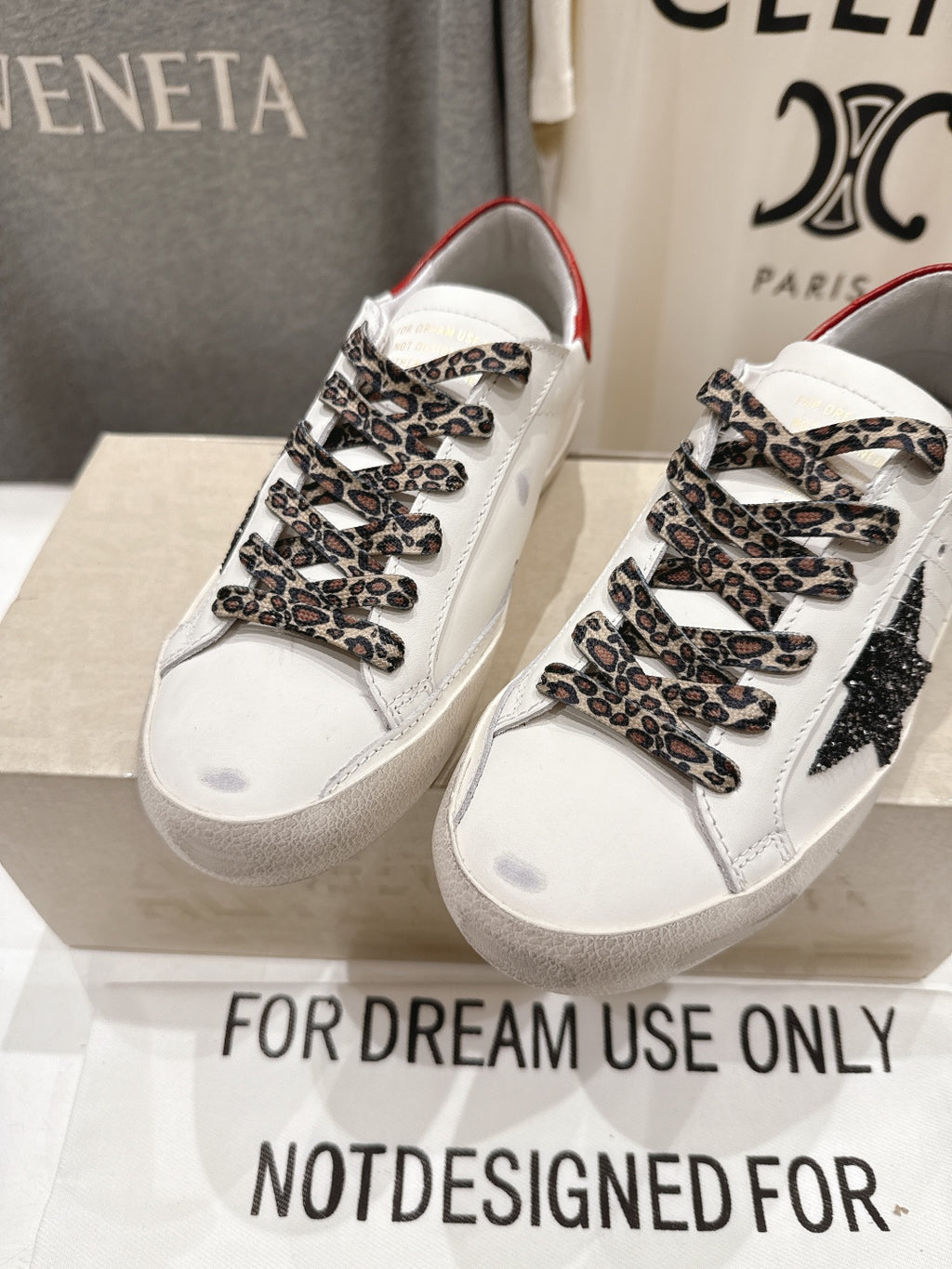 Close view of white sneakers with red collar, leopard-pattern laces, and black star detail