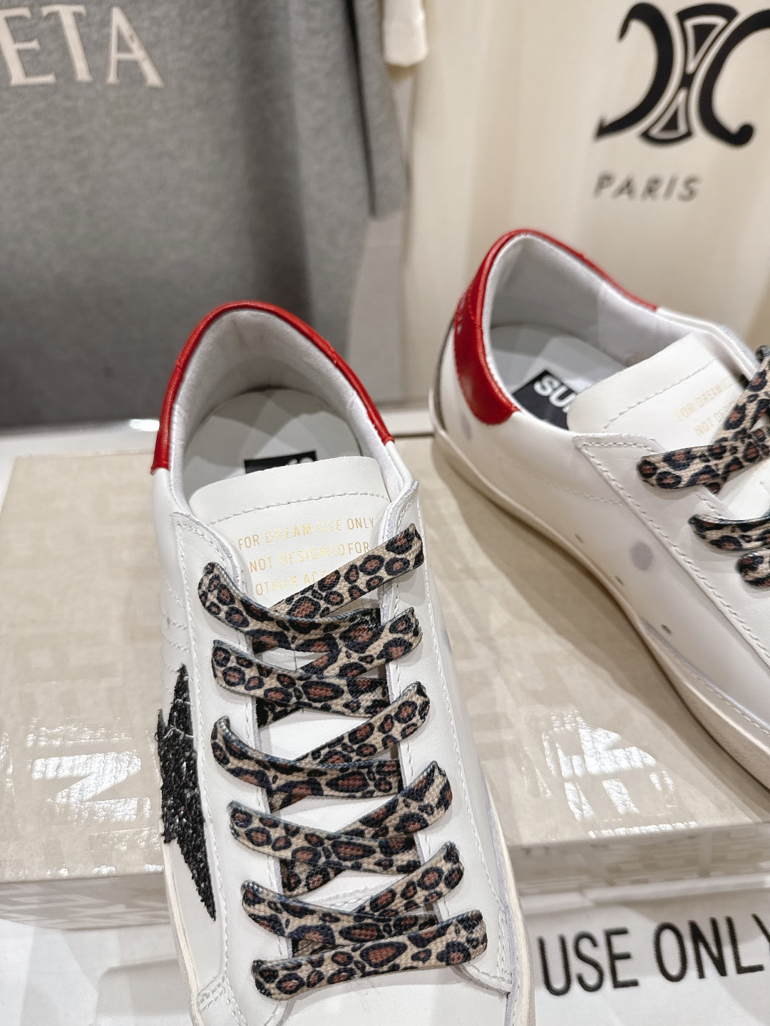 White sneaker close-up with red heel lining, leopard lace overlay, and patterned tongue