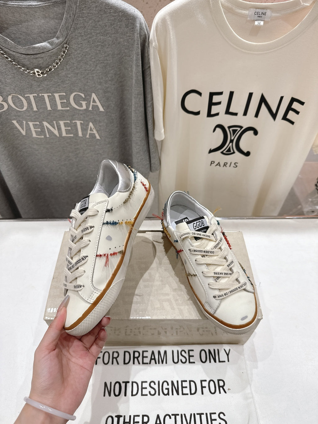White lace-up sneaker held in hand, featuring multicolor trim and tan gum sole