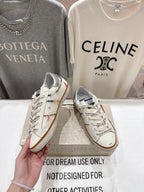 White lace-up sneaker held in hand, featuring multicolor trim and tan gum sole