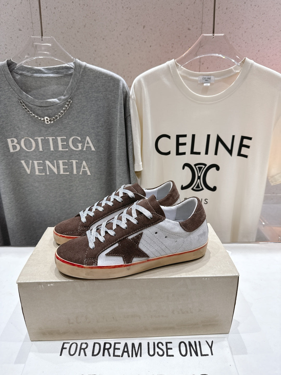 Brown, white and red-trim sneakers with white laces on display box, single shoe visible.