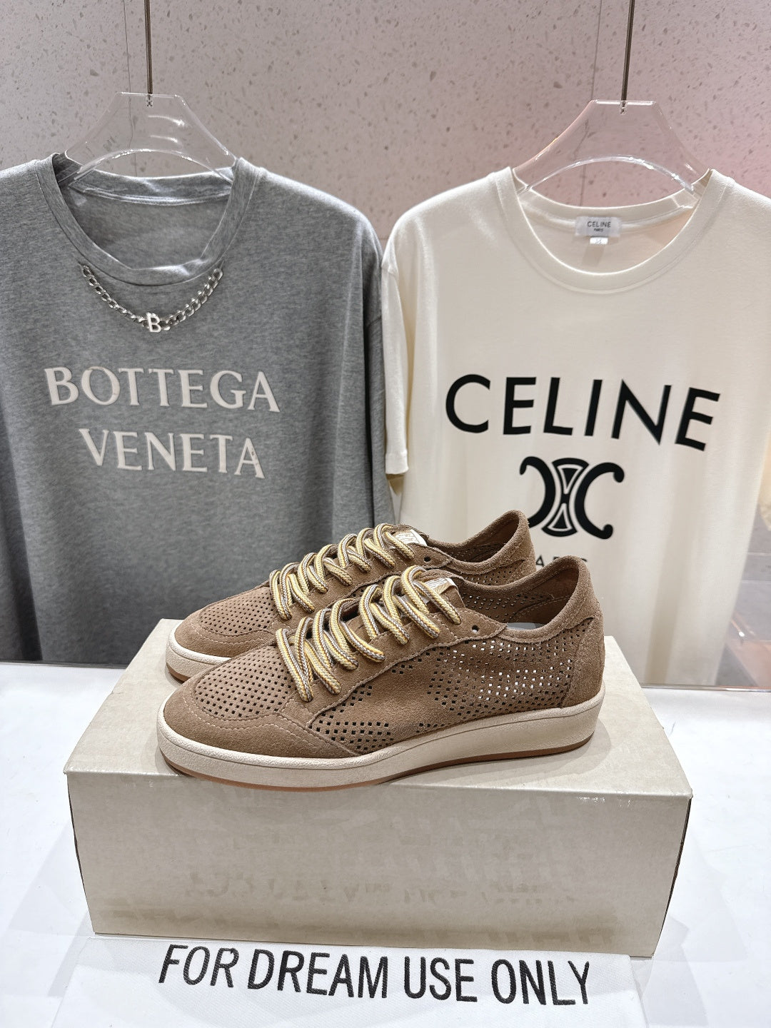 Tan perforated low-top sneakers with braided gold laces on display box
