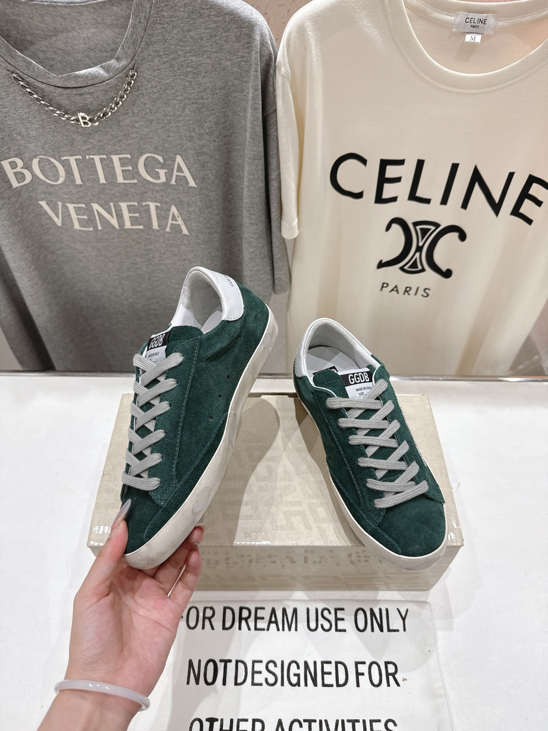 Hand holding dark green suede Golden Goose sneakers with white laces and white rubber sole