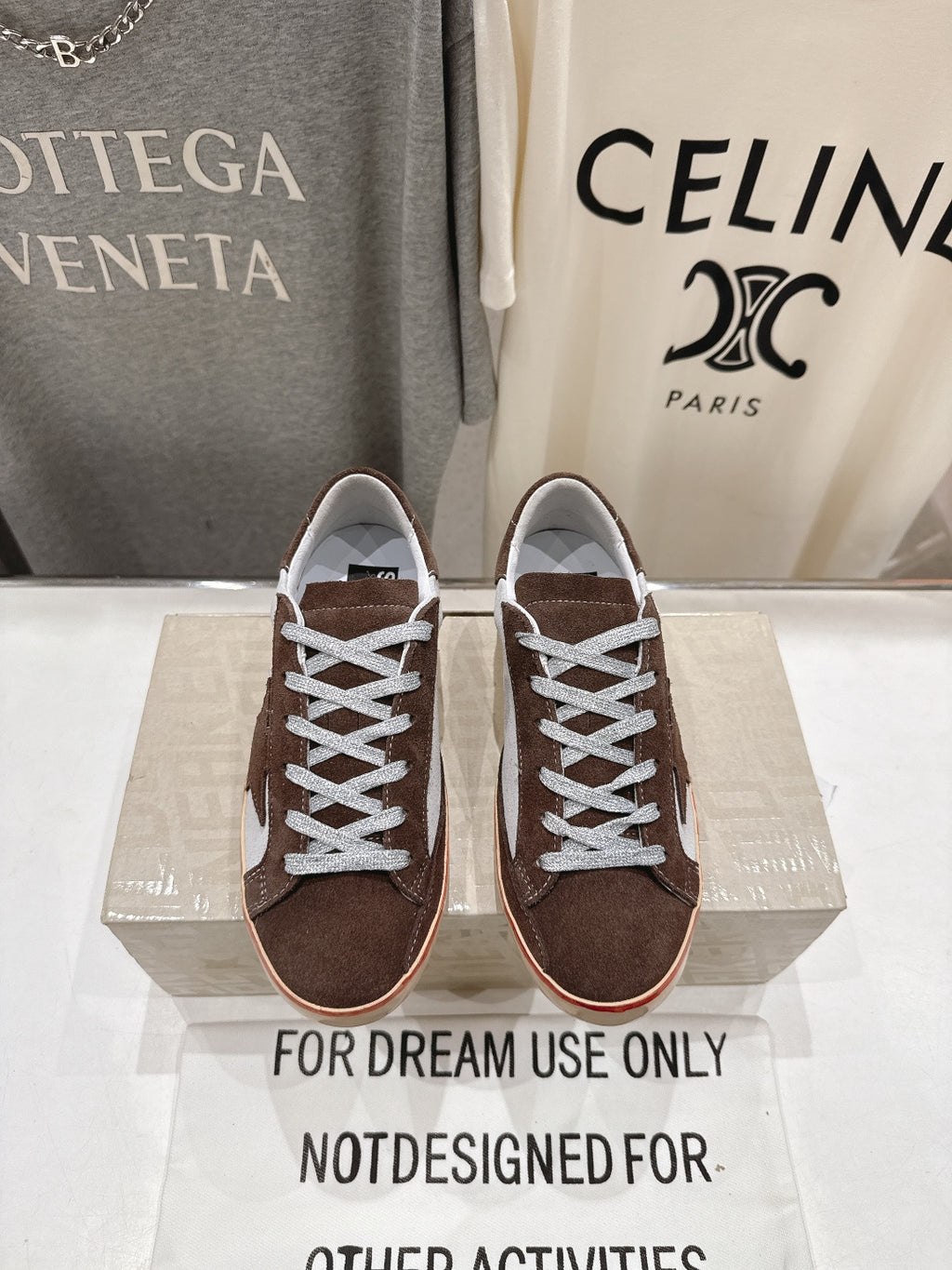 Brown suede lace-up sneakers with white laces and cream soles on a display box.