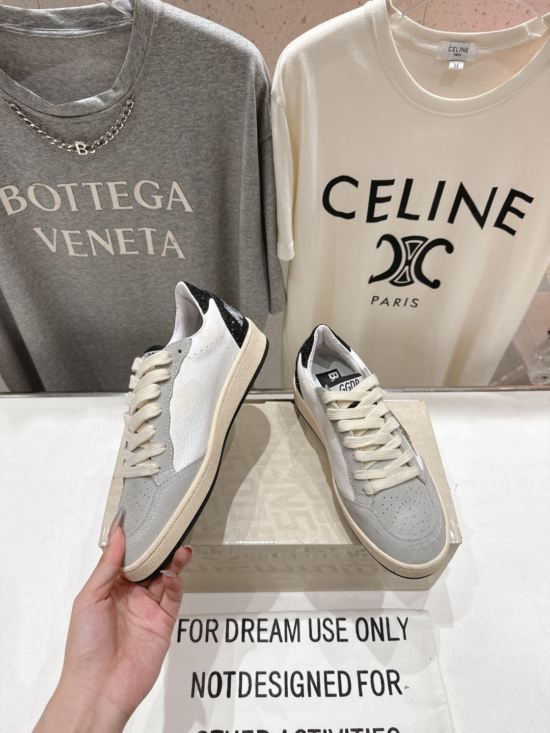 Light gray and white sneakers with cream laces, angled view in hand